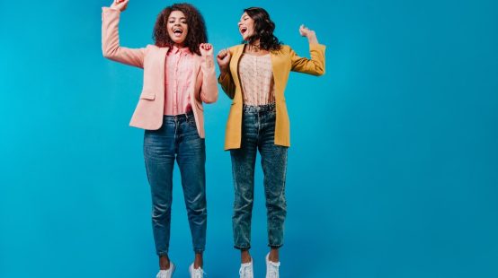 two-women-jeans-jumping-blue-wall_197531-12950